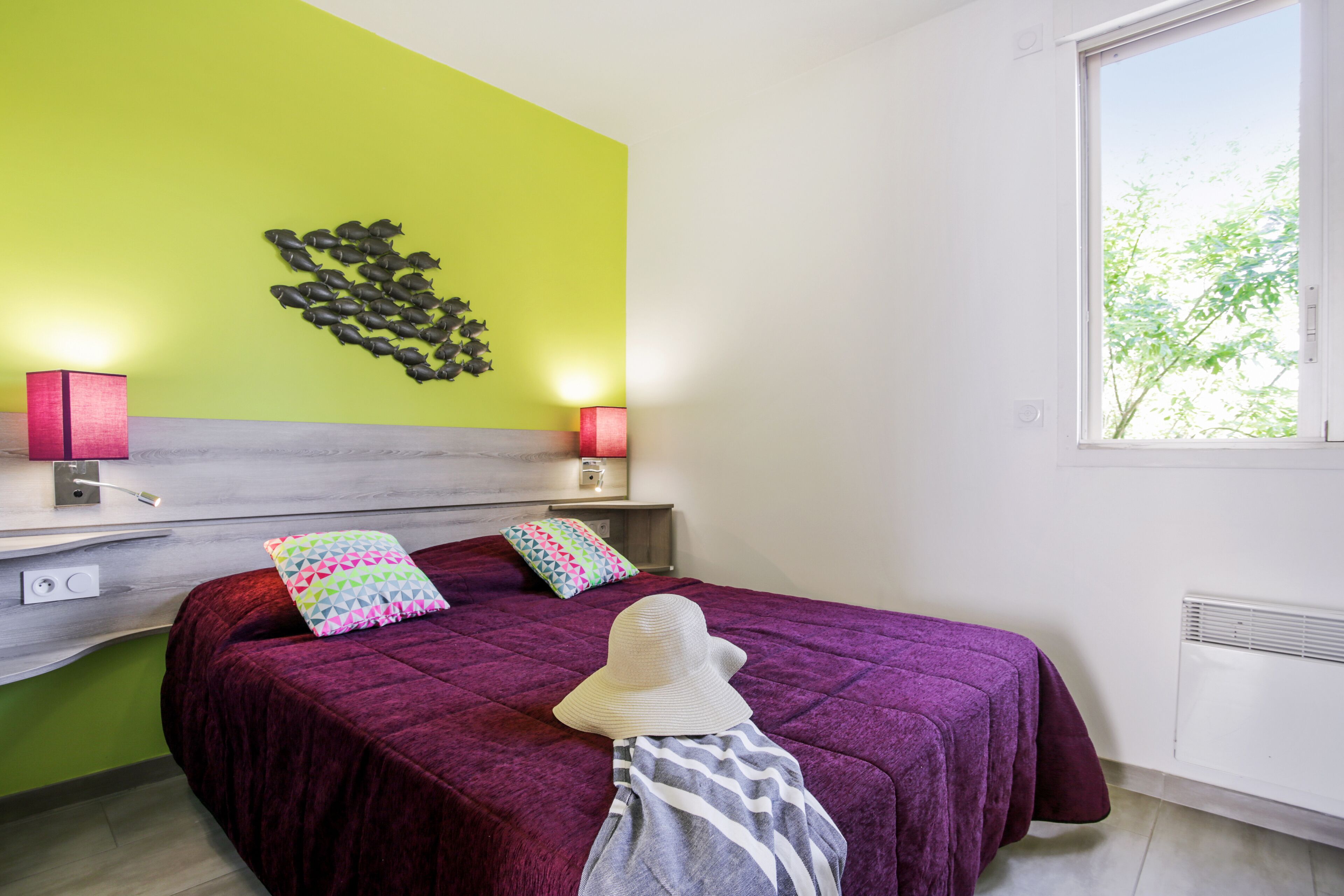 A bedroom with a bed, two bedside lamps, a window, and a wall art piece.