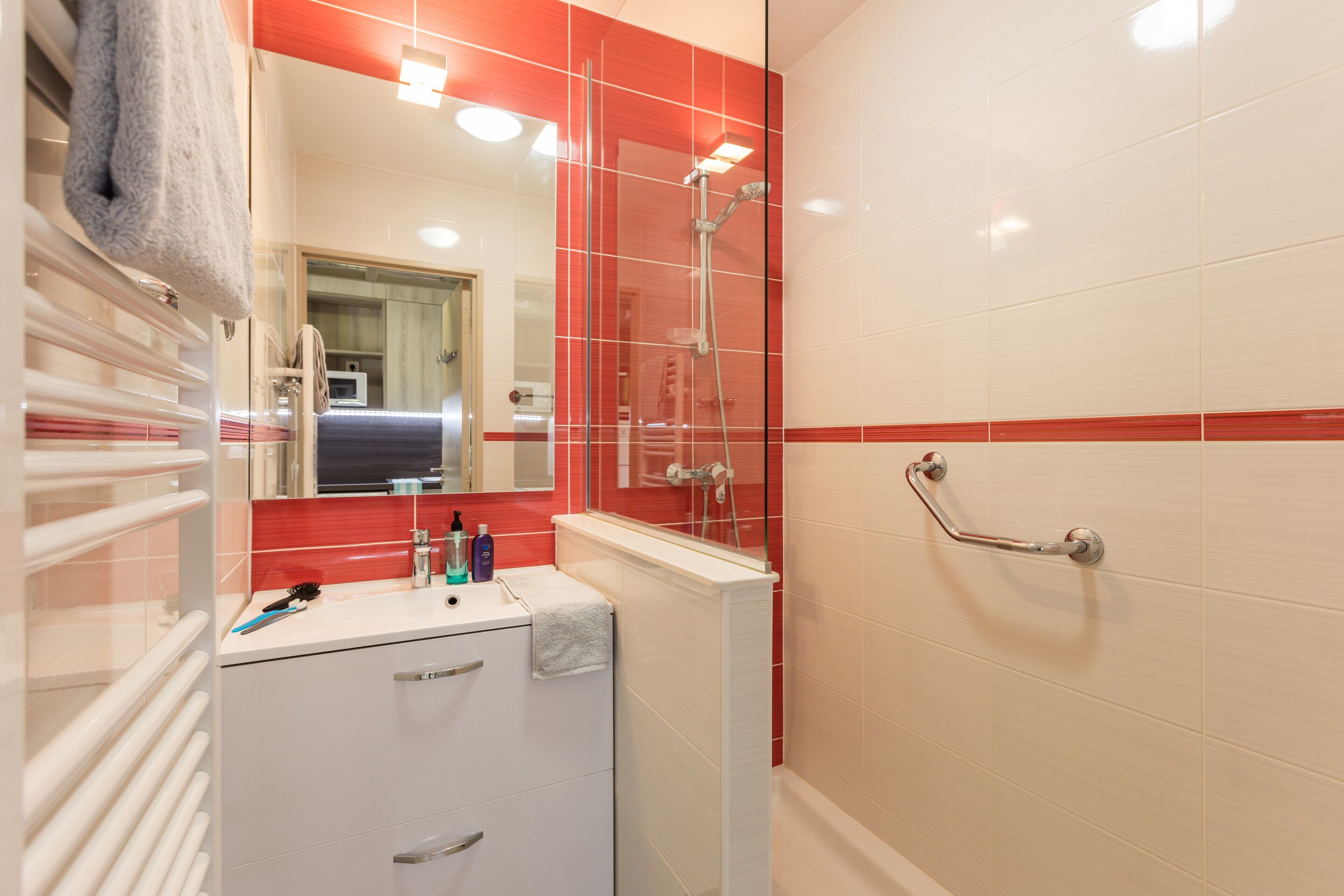 A bathroom with a glass shower enclosure, a white sink with a towel, and a handrail.