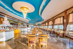 Een ruim restaurant met een lange toonbank, houten stoelen en een blauw plafond met een kroonluchter.