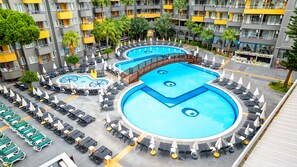 Ein Hotel mit mehreren Schwimmbecken, Liegestühlen und Sonnenschirmen.
