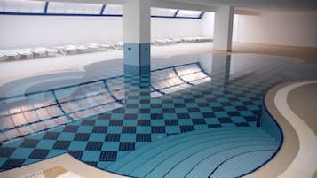 Una piscina interna con pavimento a scacchi, circondata da pareti bianche e un lucernario.