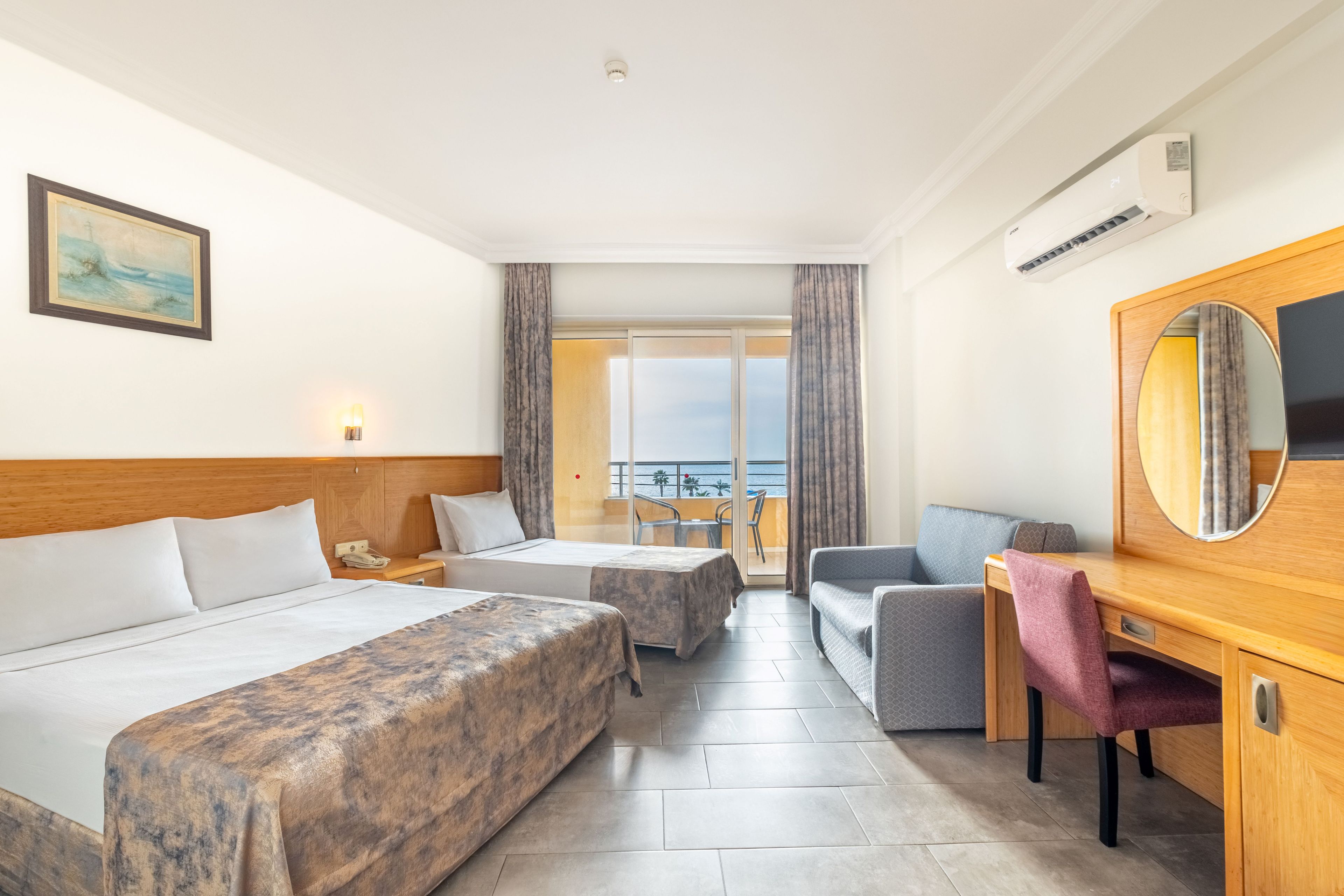 Habitación de hotel con dos camas, un escritorio, una silla, un televisor y un balcón con vistas.