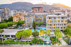 A multi-story hotel with balconies, a swimming pool, and a view of mountains.