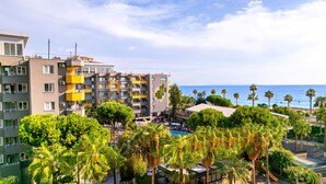Un hotel con varios pisos, balcones y una zona de piscina rodeada de palmeras.