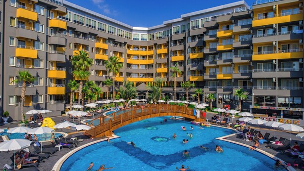 Un hotel de varios pisos con una piscina central rodeada de tumbonas y sombrillas.