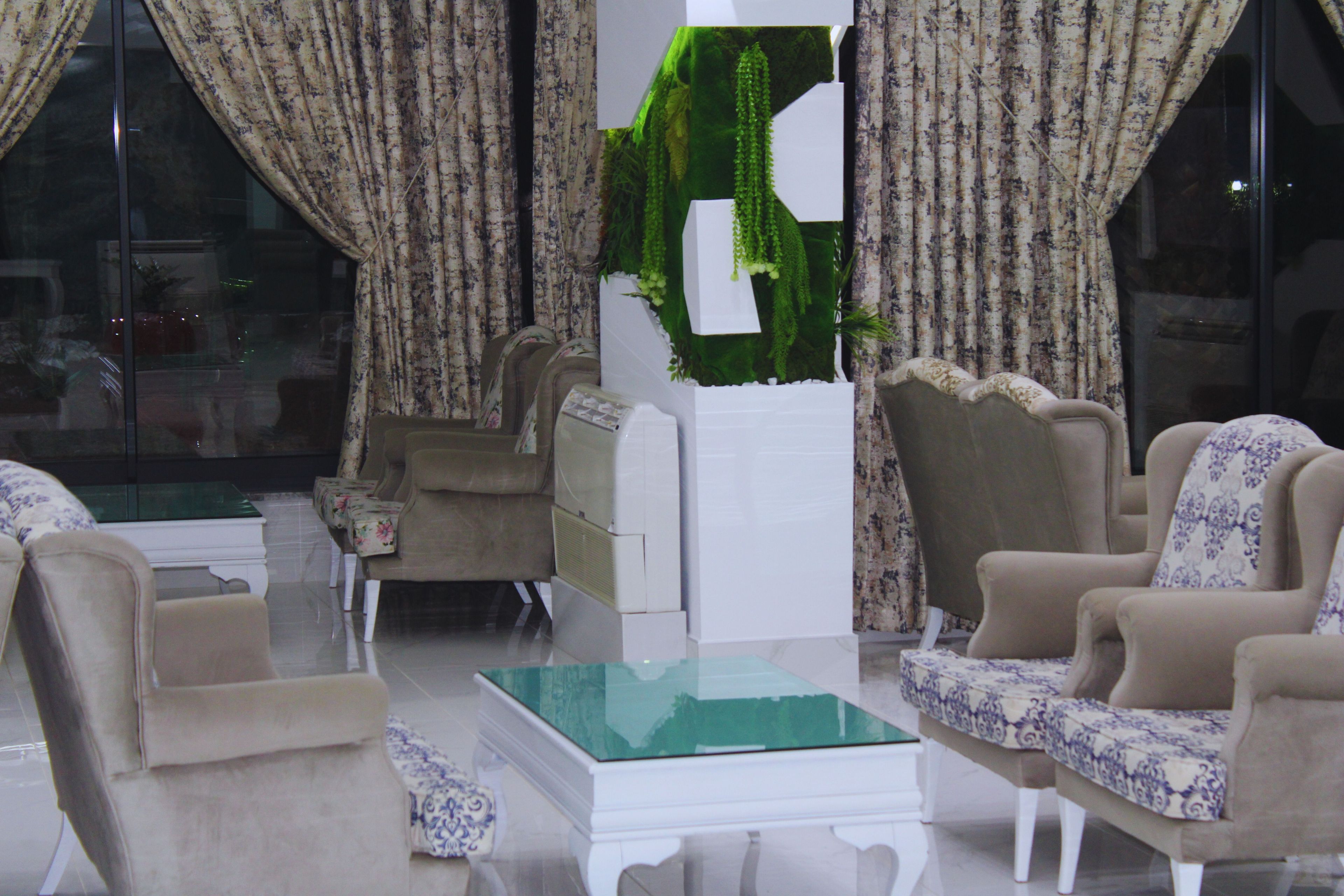 Un salon avec une table basse en verre, deux fauteuils, un canapé et des rideaux.