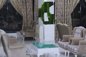 Een woonkamer met een glazen salontafel, twee fauteuils, een bank en gordijnen.