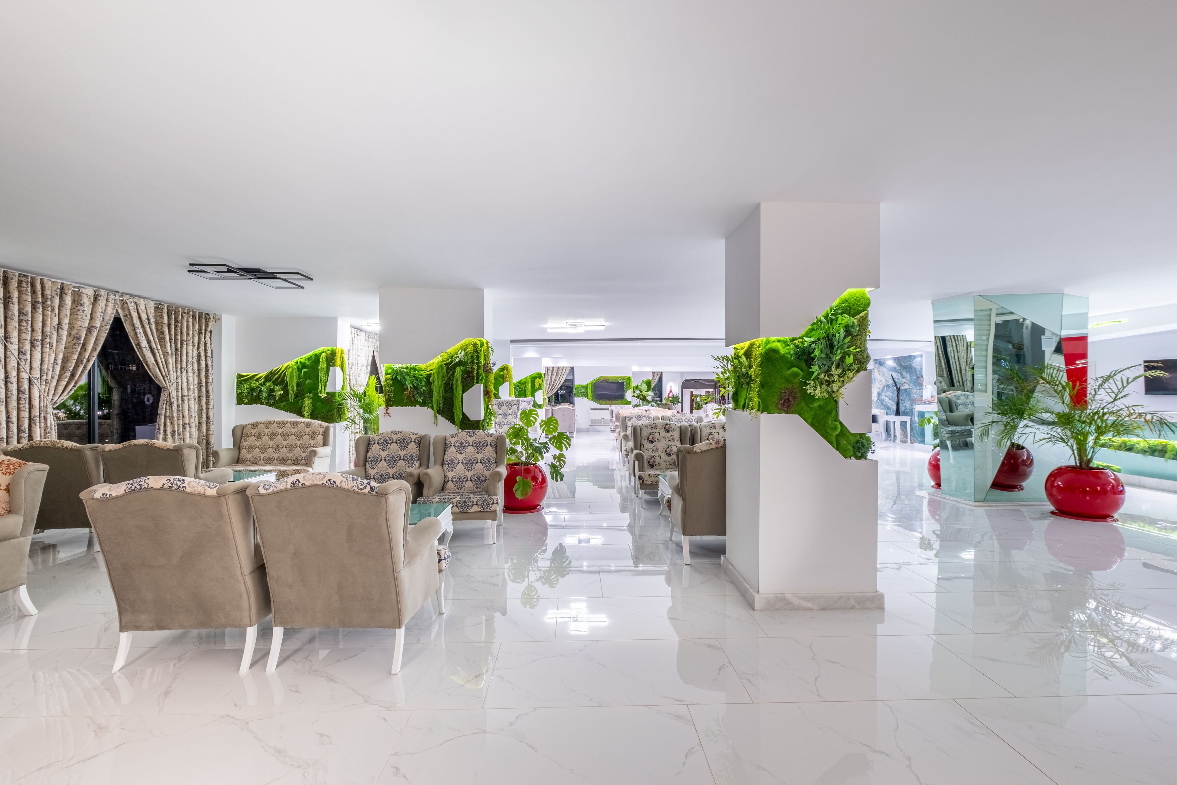 Un hall d’entrée spacieux au design moderne, avec un espace de détente central agrémenté de canapés et de fauteuils, entouré de plantes en pot et doté d’un sol en marbre poli.