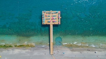 Un pontile in legno con diverse zone relax e ombrelloni, affacciato su una spiaggia con acqua turchese cristallina.