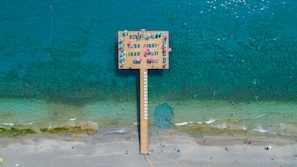 Een houten terras met meerdere zithoeken en parasols, met uitzicht op een strand met helder turquoise water.