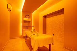 Une salle de spa équipée d’une table de massage, d’une horloge au mur et d’un mur à texture.