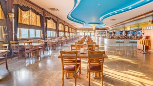 Un restaurante espacioso con filas de mesas y sillas de madera, ventanas amplias con vistas al océano y un diseño de techo azul.