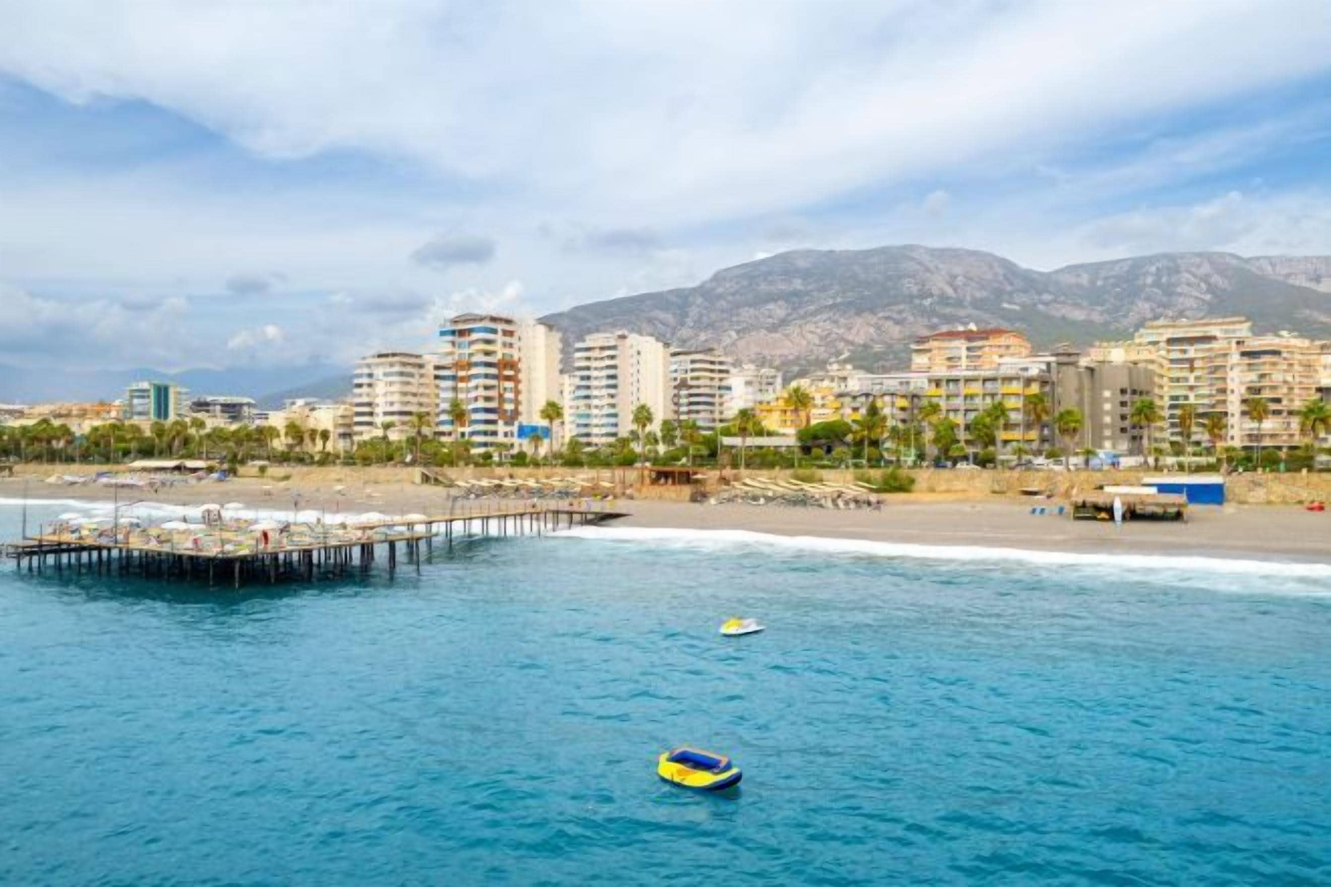 Un paisaje urbano costero con un muelle que se adentra en el mar, edificios al fondo y un cielo despejado.