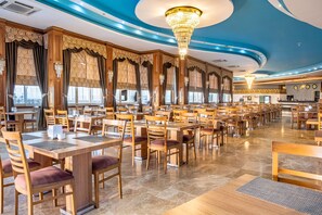 Un restaurant spacieux avec des tables et des chaises en bois, de grandes fenêtres et un lustre.