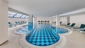 An indoor swimming pool with a blue checkered floor, surrounded by lounge chairs and a skylight above. - Senza Grand Santana Hotel (Alanya)