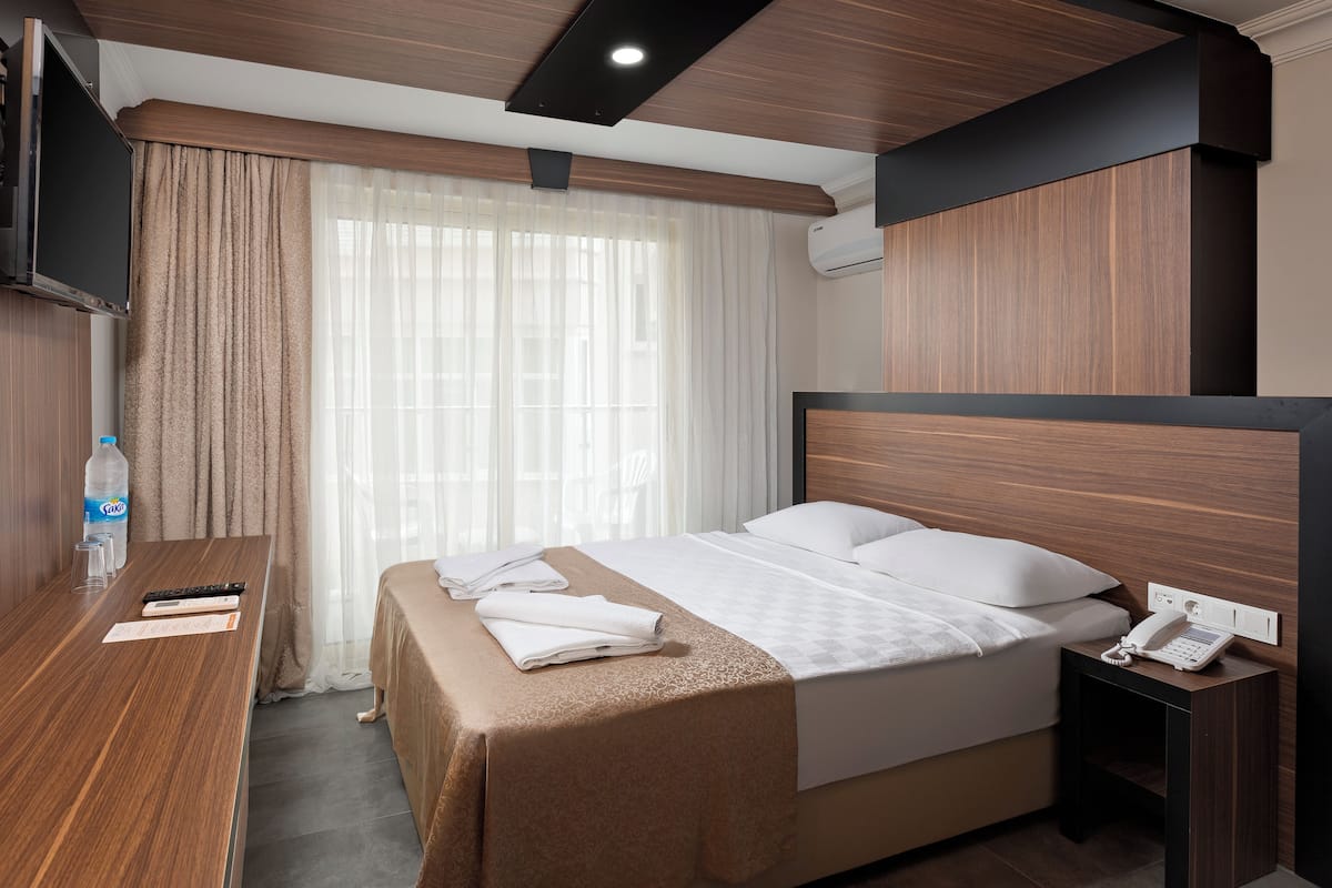 A hotel room with a bed, bedside table, and a TV mounted on the wall.