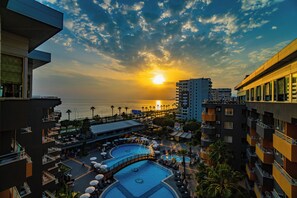 A resort with multiple swimming pools, a bridge, and a view of the sunset over the ocean.