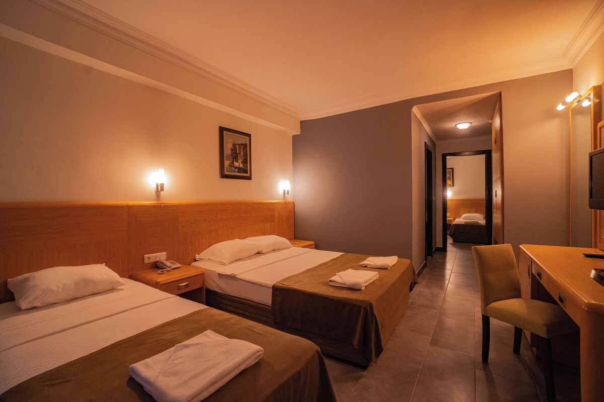 Une chambre d’hôtel avec deux lits, un bureau et une chaise. Il y a un téléphone sur la table de chevet, un tableau au mur et un miroir au-dessus du bureau.