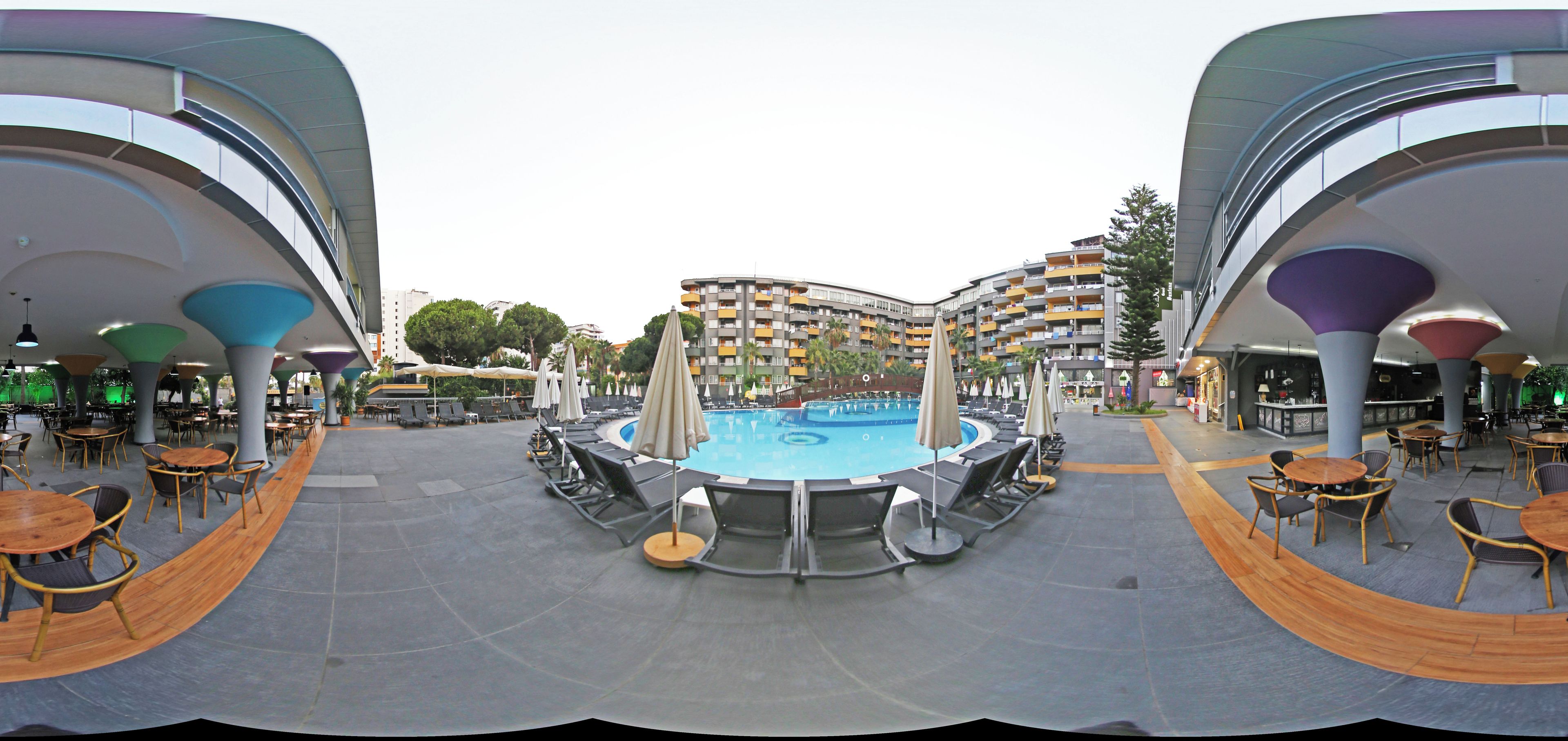 Zona de piscina con sillas de descanso y sombrillas, rodeada de edificios modernos con balcones.