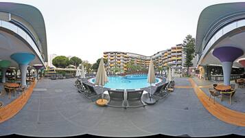 Zona de piscina con sillas de descanso y sombrillas, rodeada de edificios modernos con balcones.