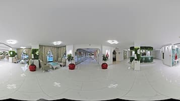 Un'ampia hall dall'arredamento moderno, con un'area salotto centrale dotata di divani e poltrone, una grande scalinata e una reception.