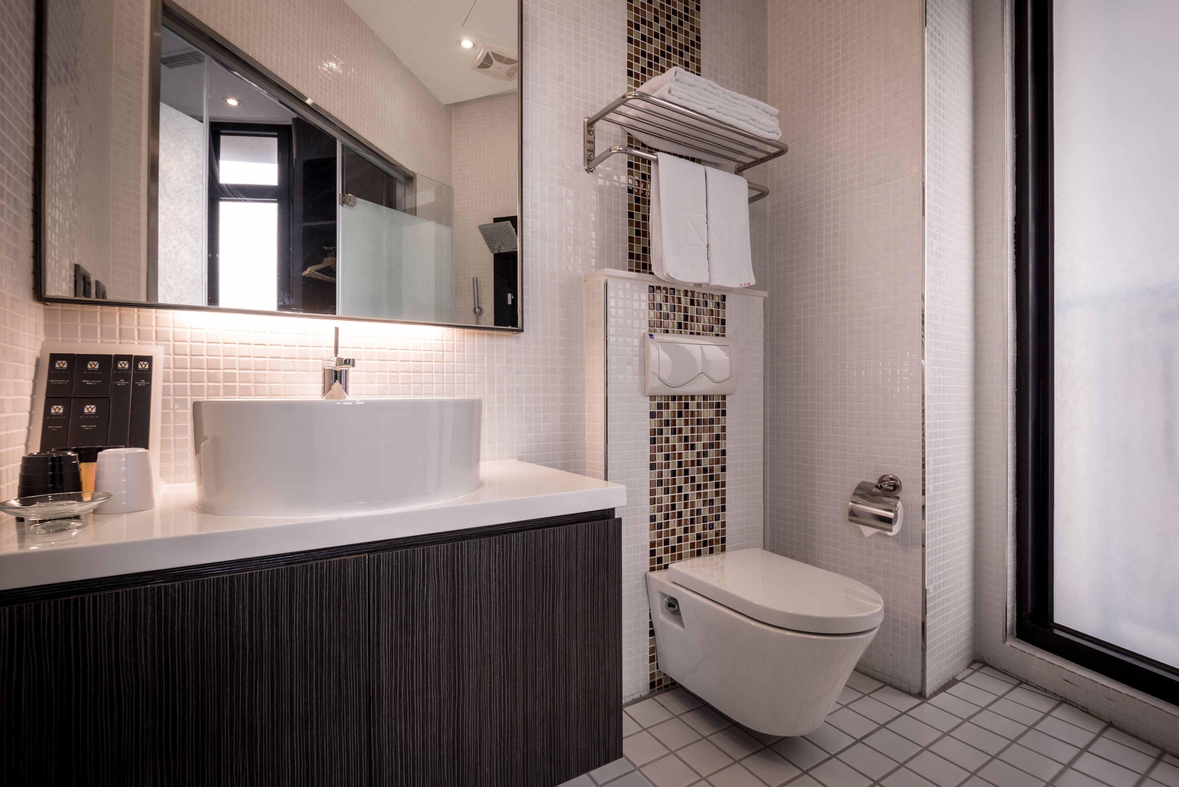 Ein modernes Badezimmer mit großem Spiegel, weißem Waschbecken, dunklem Holzschrank und Toilette sowie einer Duschkabine.