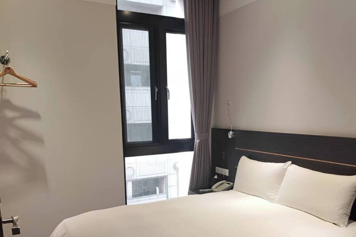 A hotel room with a large bed, a bedside table, a telephone, and a window with curtains.