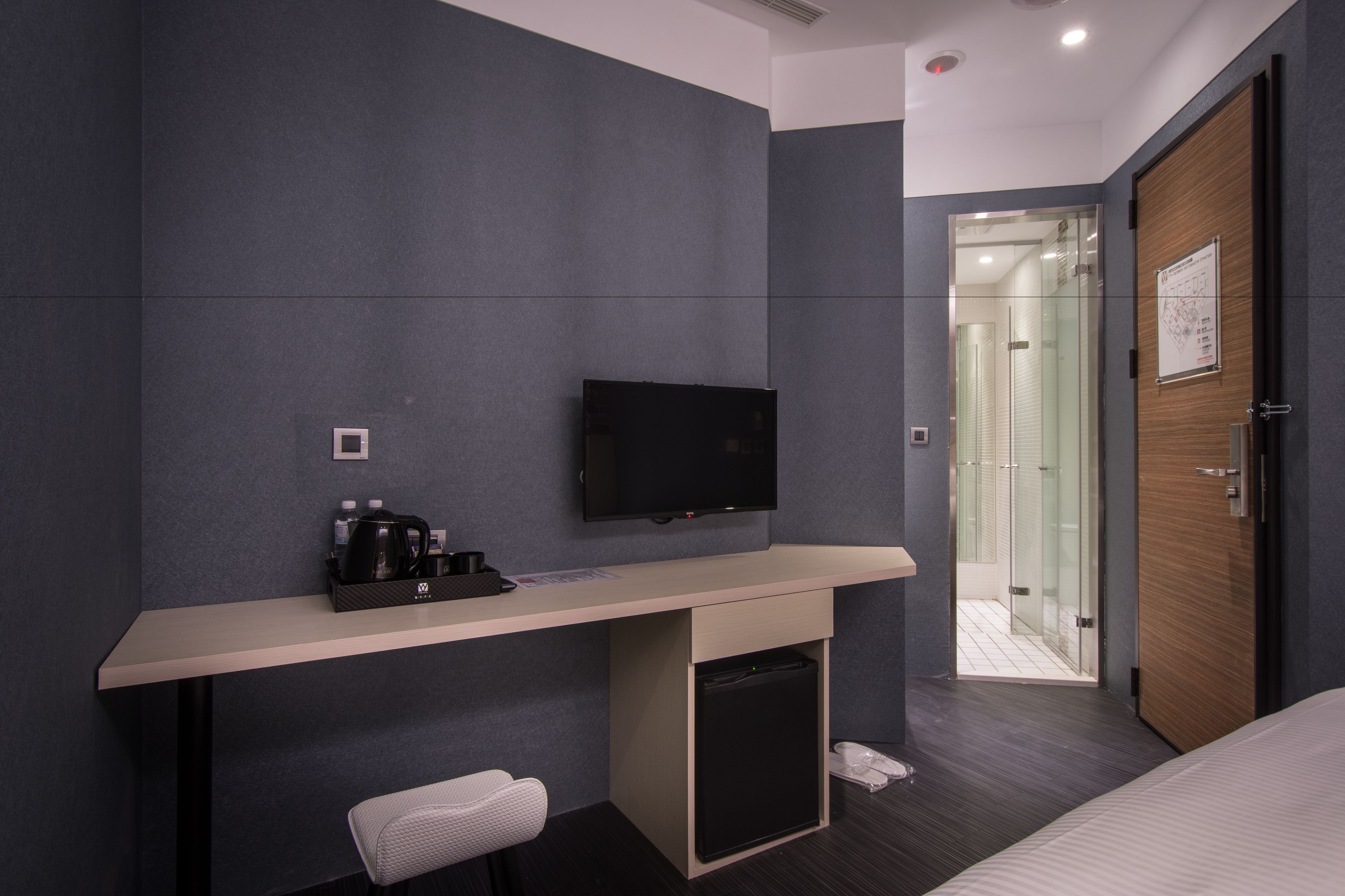Una habitación de hotel moderna con una televisión de pantalla plana, un escritorio con cafetera, un cubo de basura pequeño y una cama.