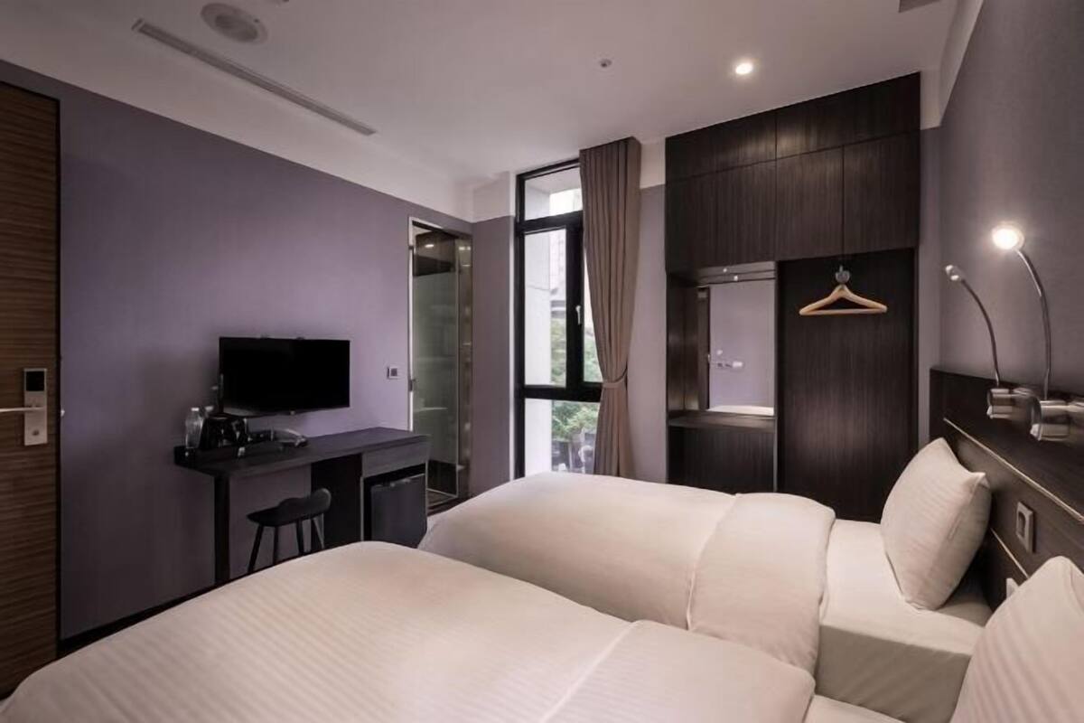 A hotel room with a bed, a desk, a TV, a mirror, and a wardrobe.