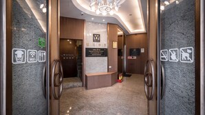 Un vestíbulo de hotel con una recepción, un candelabro y señales indicativas para servicios como WiFi y estacionamiento.