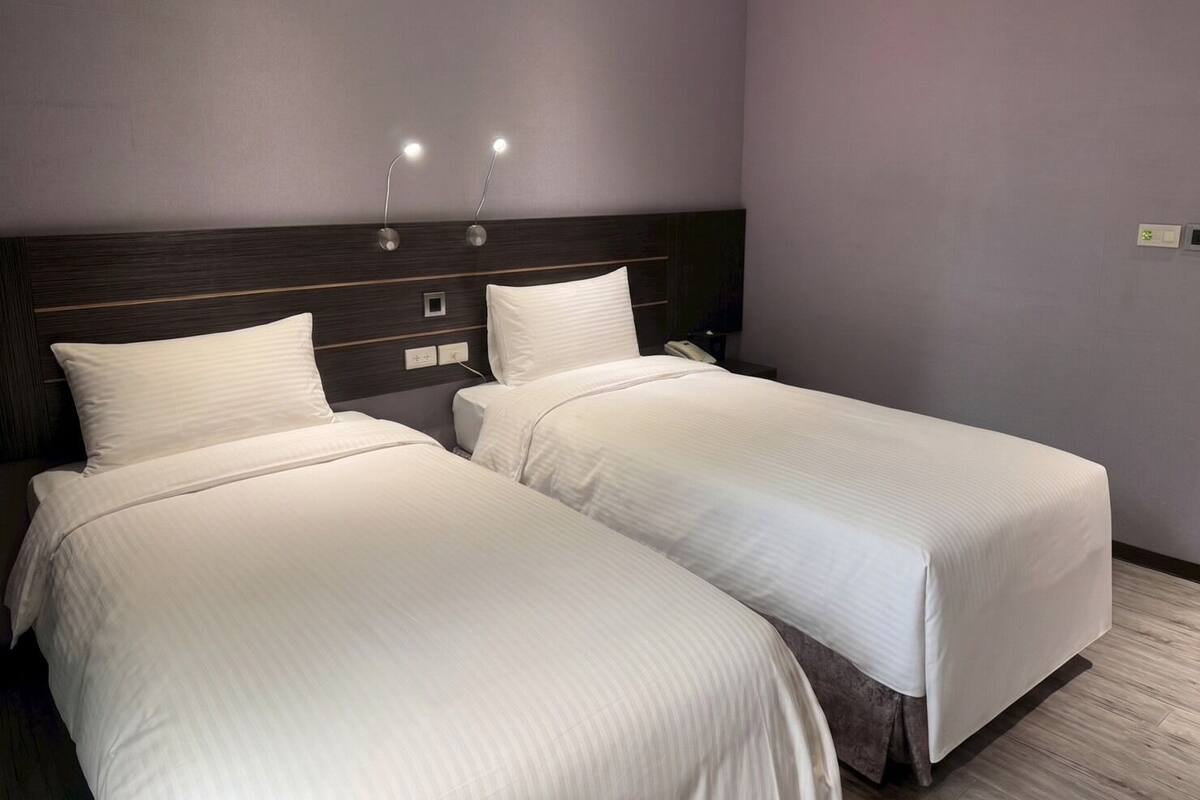 A hotel room with two beds, a dark headboard, bedside lamps, and a nightstand with a phone.