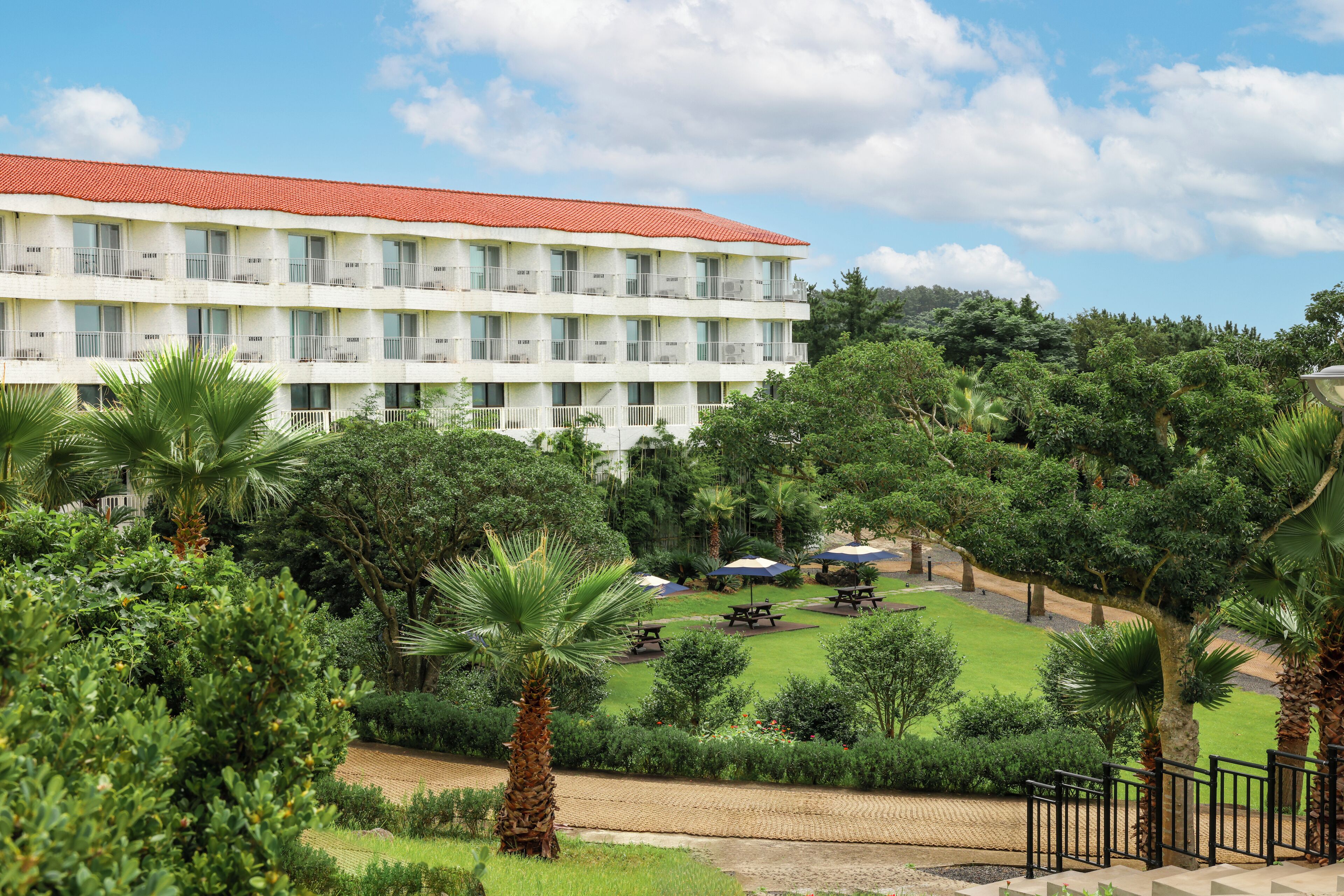 Ein mehrstöckiges Hotel mit rotem Ziegeldach, umgeben von üppiger Vegetation und Palmen.