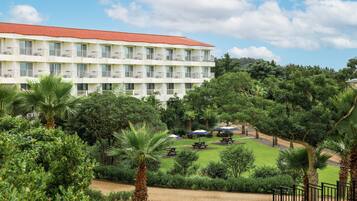 Ein mehrstöckiges Hotel mit rotem Ziegeldach, umgeben von üppiger Vegetation und Palmen.