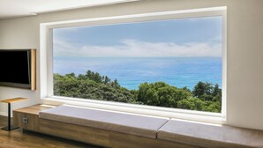 A modern room with a large window offering a view of the sea and greenery. - Kensington Resort Jeju Jungmun (Seogwipo)