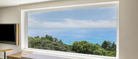 A modern room with a large window offering a view of the sea and greenery.