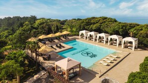 A pool area with lounge chairs, umbrellas, and cabanas, surrounded by lush greenery and overlooking a body of water. - Kensington Resort Jeju Jungmun (Seogwipo)
