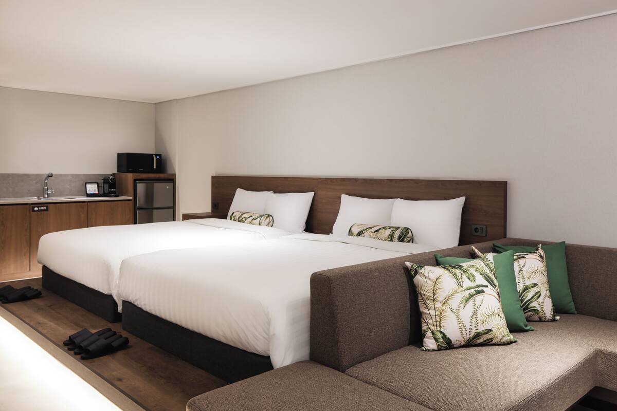 A hotel room with two beds, a sofa, a kitchenette, and a small refrigerator.