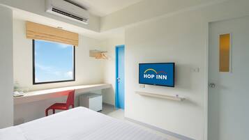 A hotel room with a bed, a desk with a chair, a television, and a window with a view of the sky.