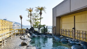 A traditional Japanese onsen with a stone bath surrounded by rocks, a wooden fence, and palm trees. - Sunmi Club (Atami)