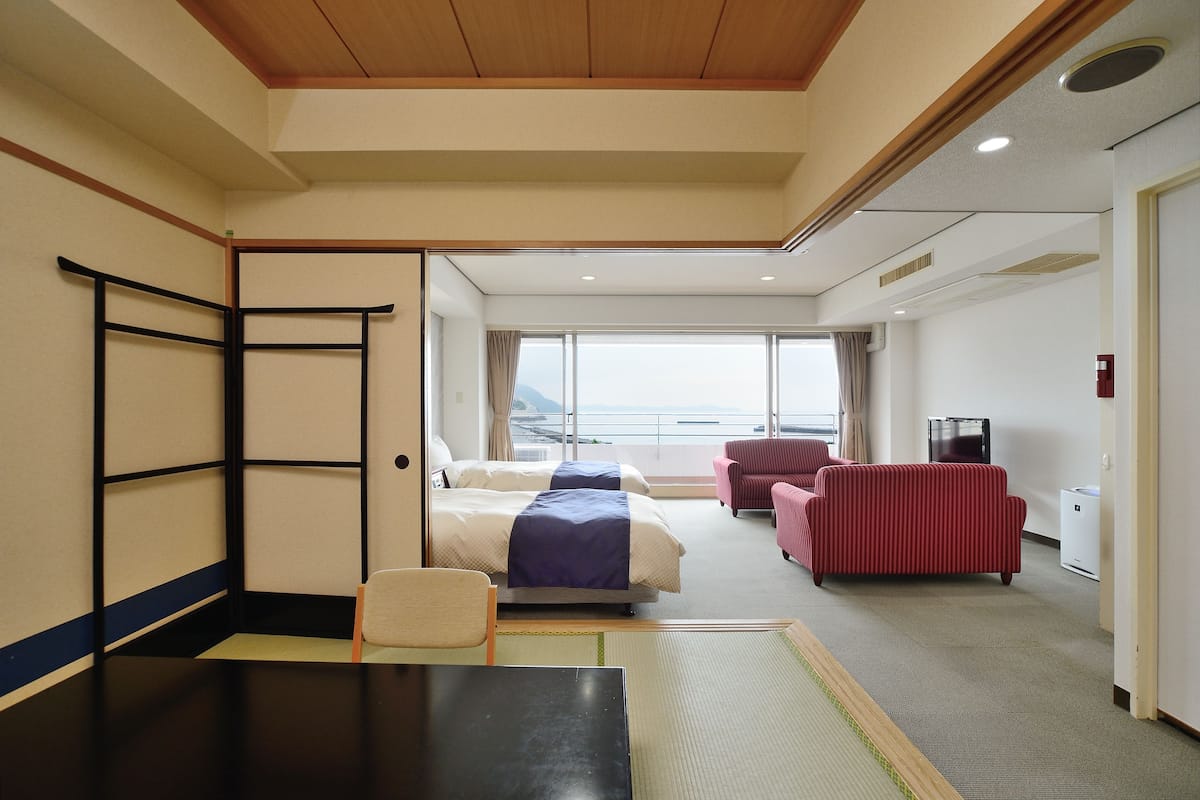 A hotel room with a bed, a desk, a chair, and a red sofa.