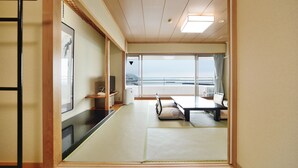 A traditional Japanese room with tatami flooring, a futon bed, a television, and a view of the sea. - Sunmi Club (Atami)