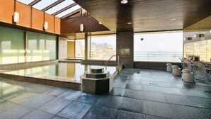 A modern indoor pool area with a view of the sea, featuring a stone fountain, seating, and a glass wall. - Sunmi Club (Atami)