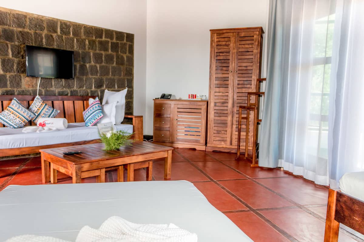 A room with a stone wall, a wooden sofa with patterned cushions, a wooden cabinet, and a bed with a white cover.