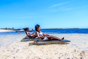 Two people relaxing on beach chairs on a sandy beach with clear blue water and a boat in the background. - Mantasaly (Antsiranana)