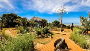 Un sendero en un jardín que lleva a una edificación con techo de paja y vistas al océano.