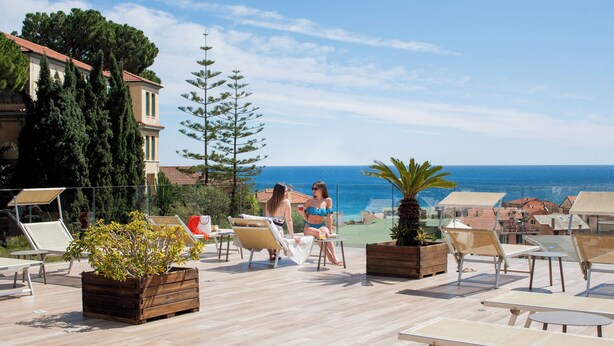 A rooftop terrace with lounge chairs, a wooden planter, and a view of the sea.