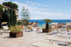 A rooftop terrace with lounge chairs, a wooden planter, and a view of the sea.