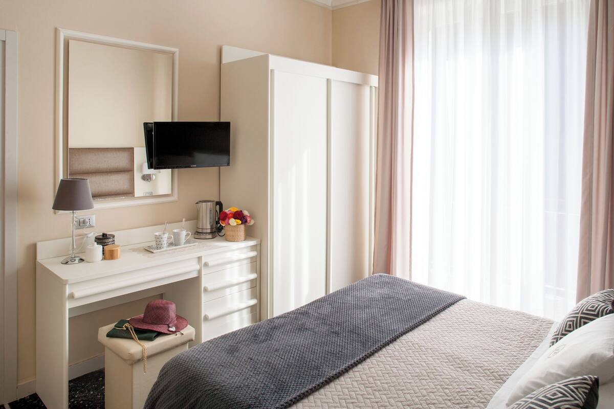 Een hotelkamer met een bed, een bureau met een televisie, een spiegel en een raam met gordijnen.