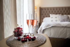 A bed with a tufted headboard, a bedside table with a glass of rose wine, and a bowl of cherries.