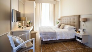 A hotel room with a bed, a desk with a chair, a TV, and a bedside table with a lamp.